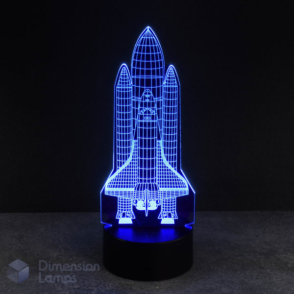 A blue LED light forms the shape of a space shuttle in this 3D lamp, set against a dark backdrop. This rocket-themed nightlight offers a unique and eye-catching option for a boys room decor.