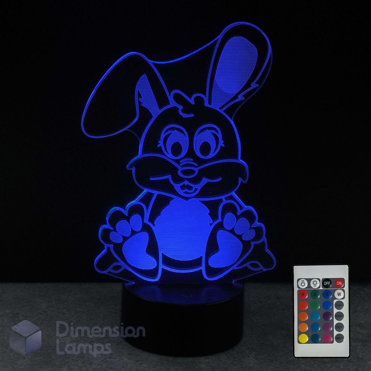 A 3D optical illusion lamp of a cartoon bunny, glowing with blue light on a black base, shown with its remote control against a black background.