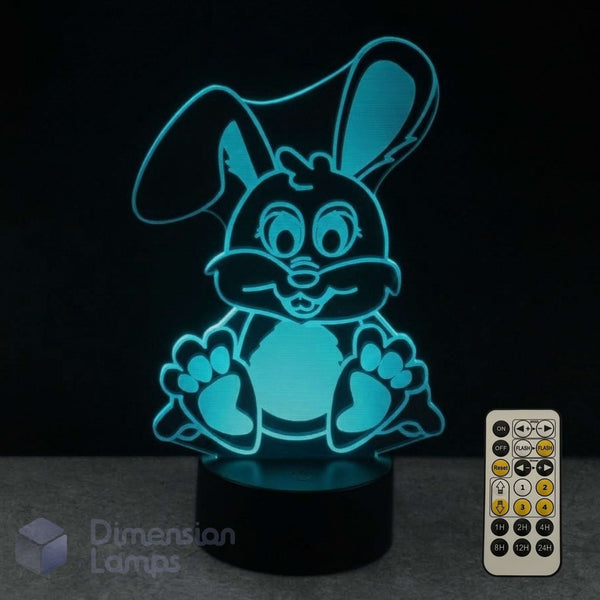 A 3D optical illusion LED lamp of a cartoon bunny glowing bright cyan n a black base. A 7 colour remote control and the Dimension Lamps watermark.
