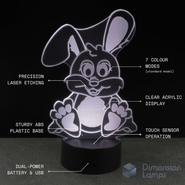 A 3D acrylic rabbit-shaped night light glowing on a black base, with text callouts highlighting features such as laser etching, clear acrylic display, sturdy plastic base, touch sensor operation, dual-power battery, and 7 colour modes. The brand name 'Dimension Lamps' appears in the bottom right corner.
