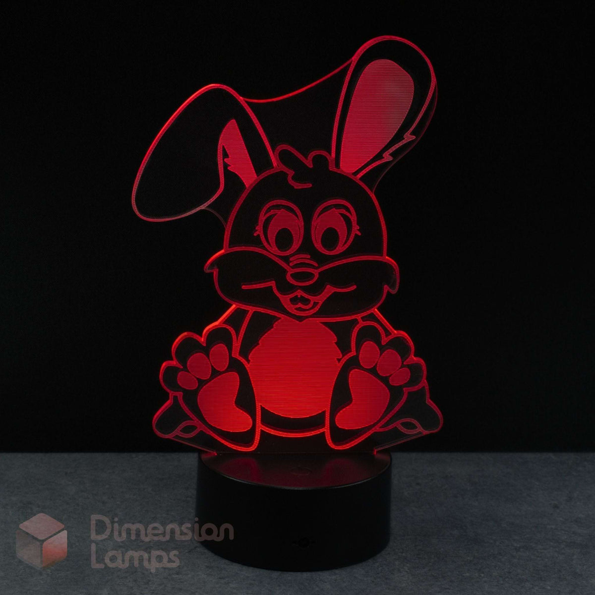 A red 3D acrylic LED night light of a cartoon bunny rabbit on a black base against a dark background with a Dimension Lamps watermark in the corner.