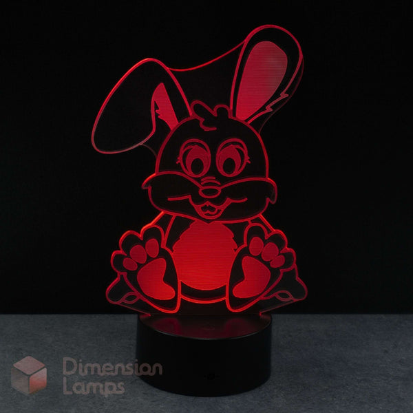 A red 3D acrylic LED night light of a cartoon bunny rabbit on a black base against a dark background with a Dimension Lamps watermark in the corner.