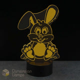 A 3D acrylic LED night light shaped like a cartoon bunny, featuring a yellow design on a black cylindrical base, set against a dark background.
