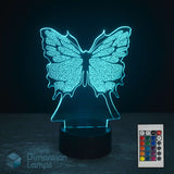 A 3D optical illusion LED night light shaped like a butterfly, glowing with a cyan light, shown on a dark surface with its remote control in the bottom right corner. Butterfly lamp gift. 