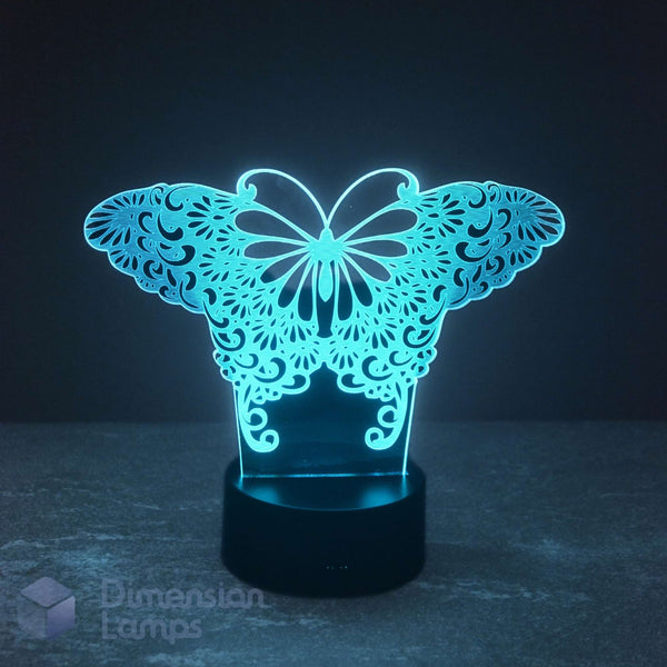 A 3D optical illusion LED night light shaped like a butterfly with intricate wing patterns, glowing with a bright cyan-blue light from a black circular base on a dark surface.
