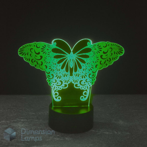 A 3D acrylic optical illusion night light shaped like a butterfly with intricate lace-like wing patterns, glowing green on a black base against a dark background. A 'Dimension Lamps' watermark is visible in the bottom-left corner.