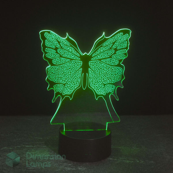 A 3D optical illusion lamp shaped like a butterfly, glowing with a bright green light from a black cylindrical base, set against a dark background. Girls night light.