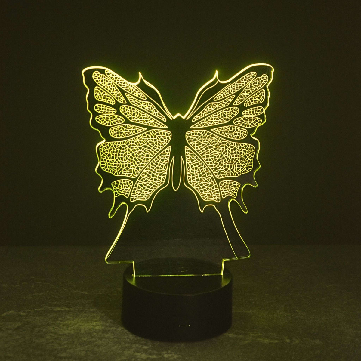 A glowing butterfly-shaped LED night light with an intricate butterfly pattern, mounted on a round black base and emitting a warm yellow light against a dark background. Girls gift idea. 