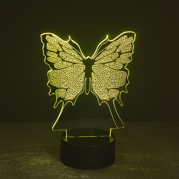 A glowing butterfly-shaped LED night light with an intricate butterfly pattern, mounted on a round black base and emitting a warm yellow light against a dark background. Girls gift idea. 