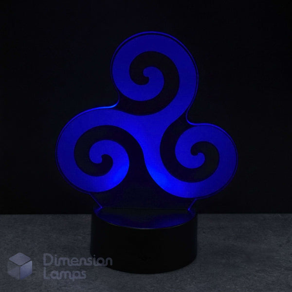A 3D optical illusion night light with a blue glowing Celtic triskelion design on a black cylindrical base, set against a dark background. Celtic art gift.