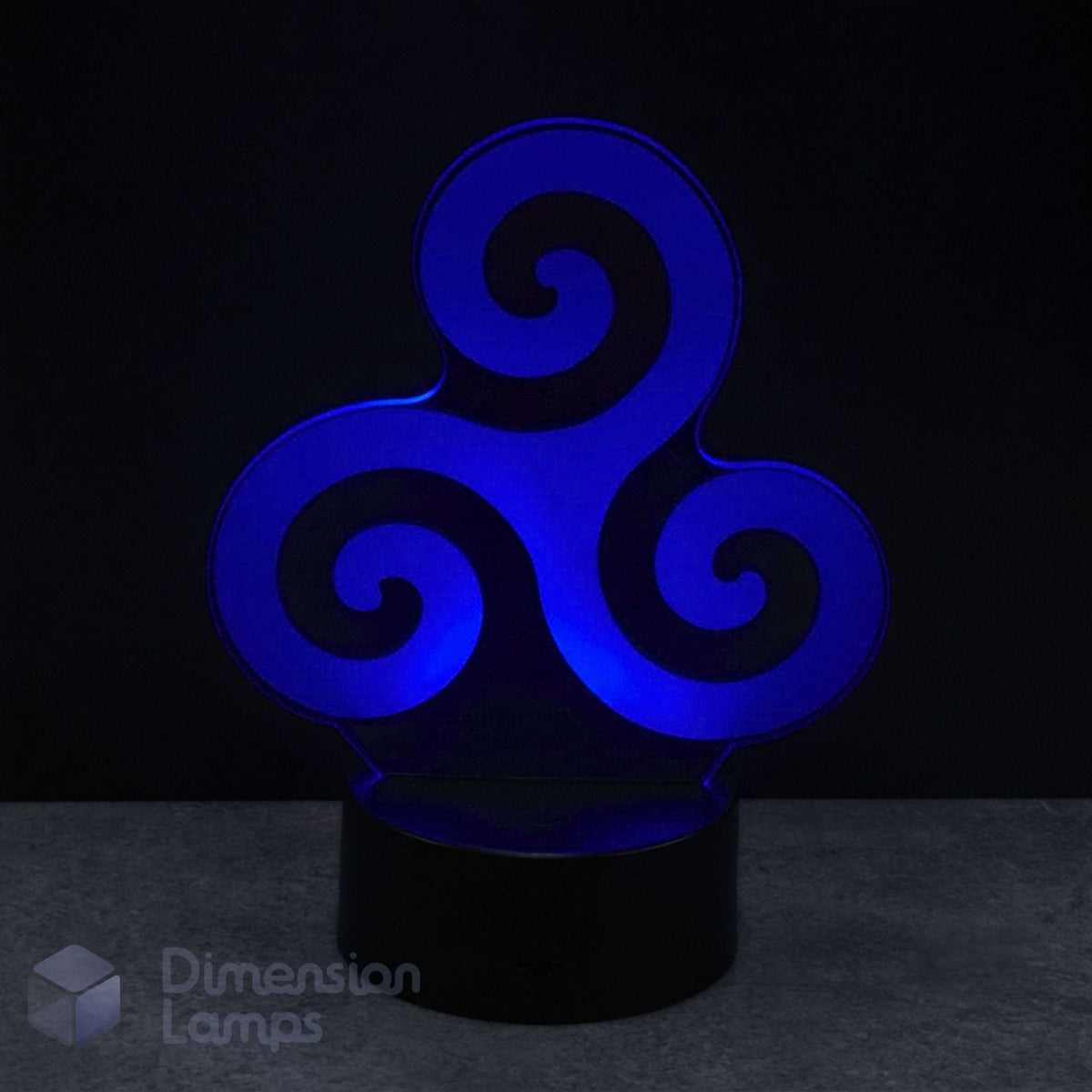 A 3D optical illusion night light with a blue glowing Celtic triskelion design on a black cylindrical base, set against a dark background. Celtic art gift.