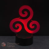 A red 3D optical illusion LED night light with a triskelion spiral design, resting on a black cylindrical base against a dark background. Celtic history gift idea. 