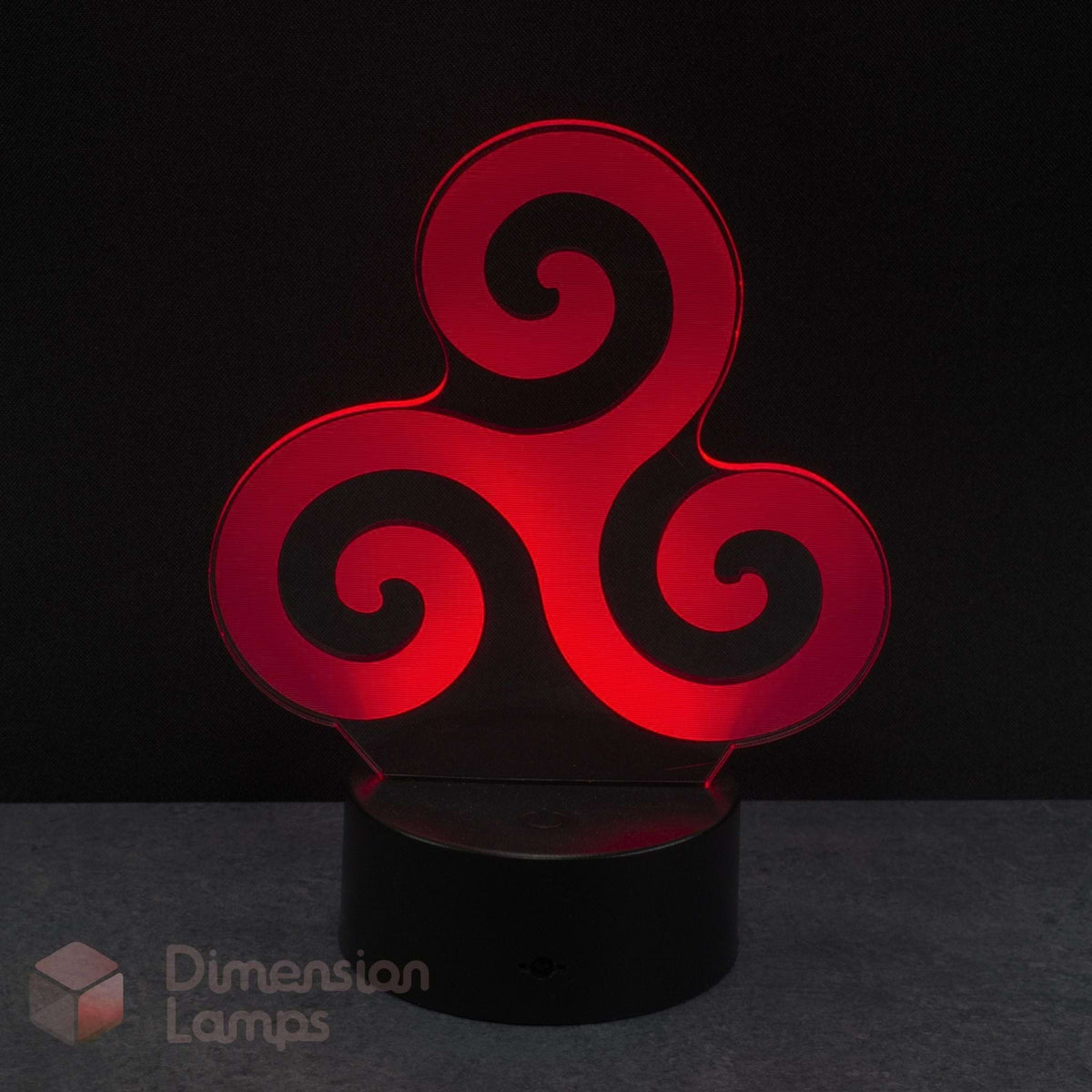 A red 3D optical illusion LED night light with a triskelion spiral design, resting on a black cylindrical base against a dark background. Celtic history gift idea. 