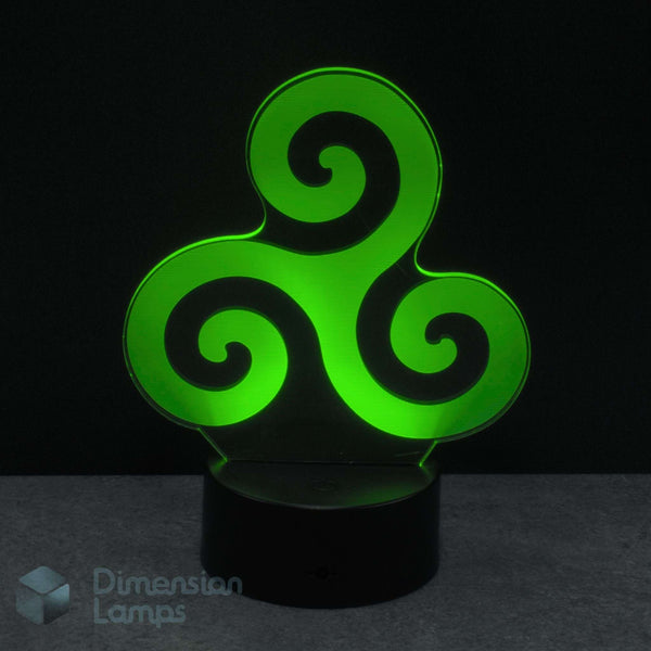 A 3D optical illusion LED night light featuring a glowing green Celtic triskelion symbol on a black cylindrical base, set against a dark background. Spiritual Balance: Unity of mind, body, and spirit or perpetual motion and progress.