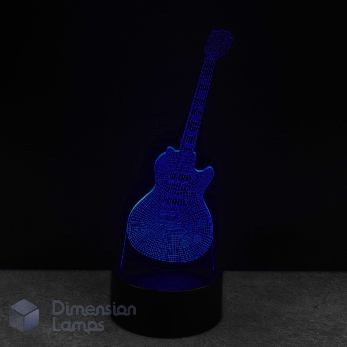 A 3D laser-etched guitar-shaped LED night light glowing in blue, set on a black cylindrical base against a dark background. A 'Dimension Lamps' logo is visible in the bottom-left corner.