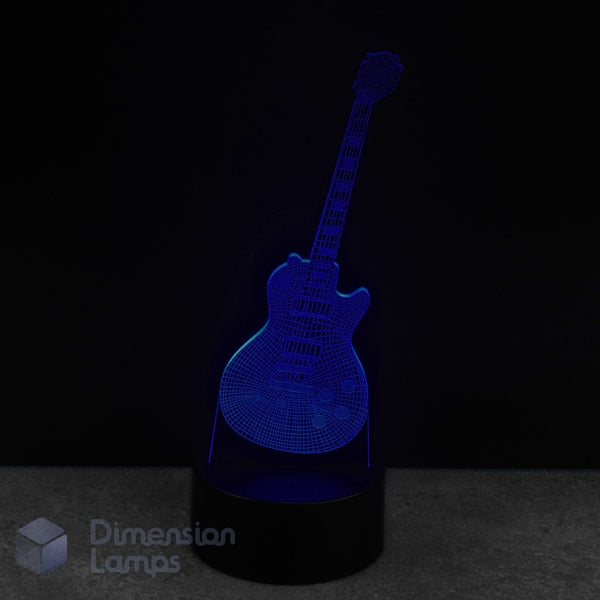 A 3D laser-etched guitar-shaped LED night light glowing in blue, set on a black cylindrical base against a dark background. A 'Dimension Lamps' logo is visible in the bottom-left corner.