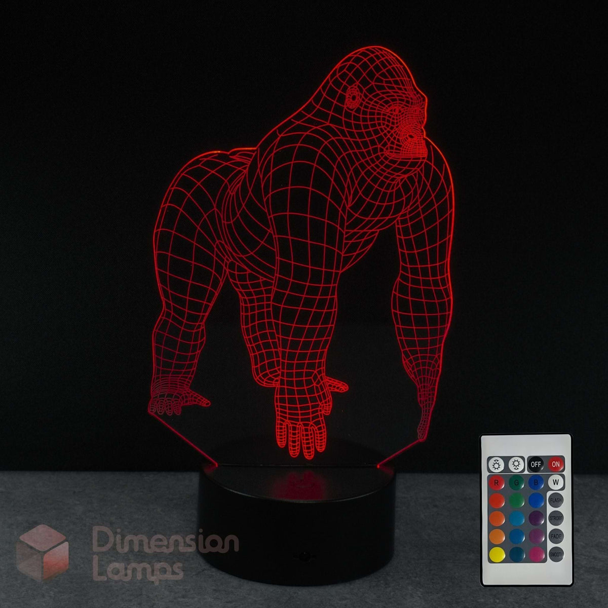 A gorilla 3D illusion LED lamp, glowing with red light, on a black base with a 16 colour remote control on a dark background. Zoologist gift idea. 