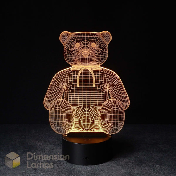 A teddy bear 3D optical illusion LED lamp, glowing warm yellow on a dark background. Formed by intricate wireframe lines, sitting on a black base.