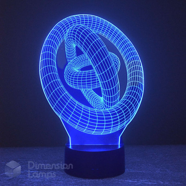 A 3D optical illusion LED night light shaped like a knot, glowing with a bright blue light on a dark base against a dark background. A 'Dimension Lamps' watermark is visible in the lower-left corner.