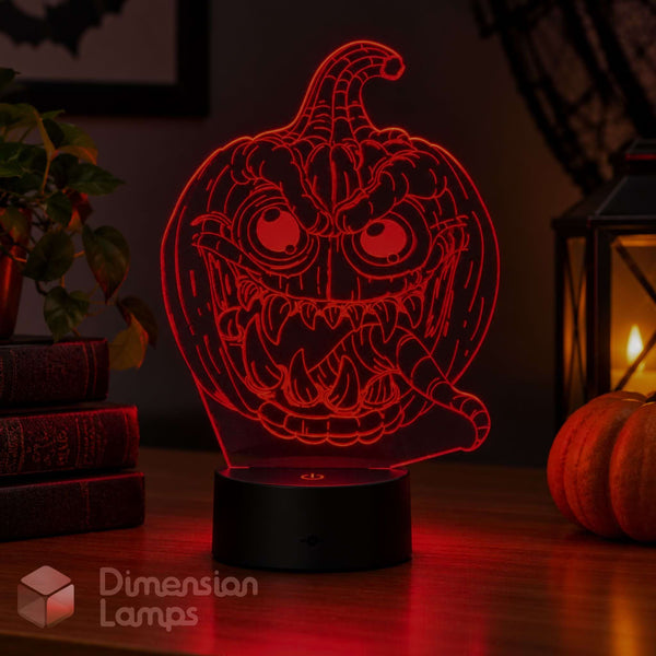 A red glowing 3D acrylic pumpkin light with a spooky jack-o'-lantern face. Styled for Halloween with a plant, books, and a lantern in the background.