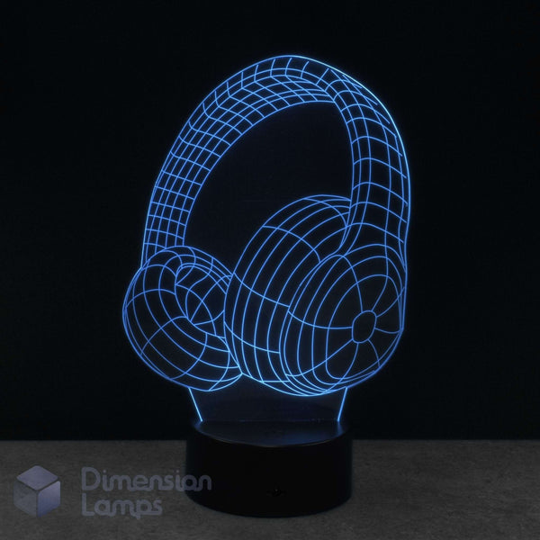 A 3D optical illusion LED night light shaped like over-ear headphones, glowing with a blue wireframe effect on a black base against a dark background.
