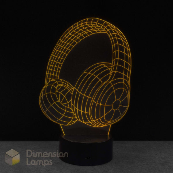 A 3D optical illusion lamp of over-ear headphones, glowing with a warm yellow wireframe outline on a black circular base. Teens music gift idea. 