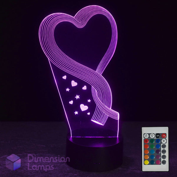 A 3D optical illusion LED night light shaped like a heart, glowing with purple light on a black base, shown with its white remote control against a black background.