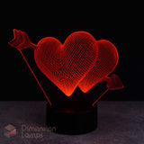 A 3D optical illusion LED night light featuring two glowing red hearts pierced by an arrow, mounted on a black cylindrical base against a dark background.