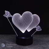 A 3D optical illusion LED night light featuring two interlocking glowing wireframe hearts pierced by an arrow, mounted on a black cylindrical base against a dark background.