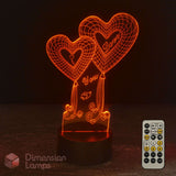 An illuminated 3D optical illusion night light shaped like two heart balloons with the words 'I Love You' on a dark base, shown with a remote control on a dark background. The brand name 'Dimension Lamps' appears in the lower-left corner.