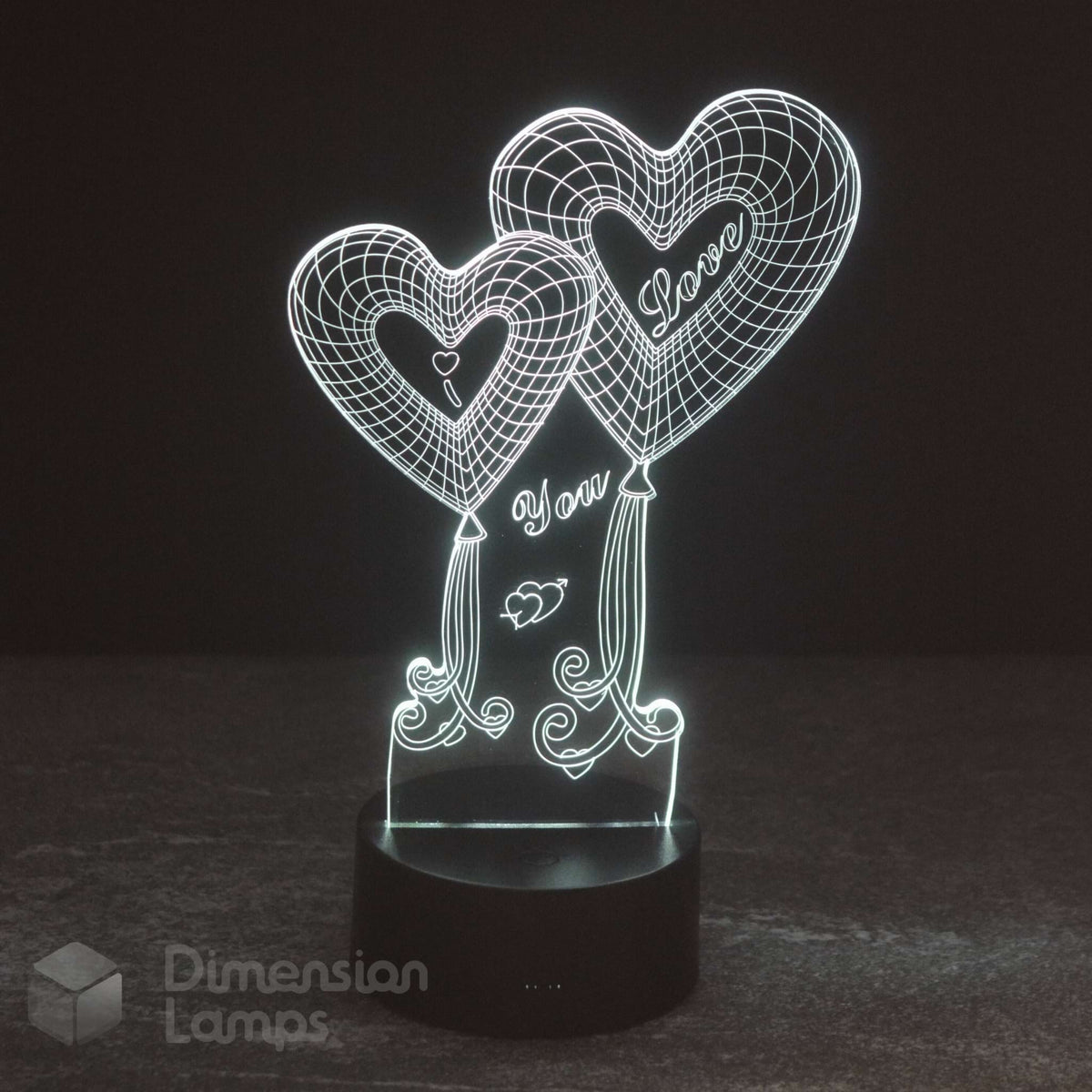 A 3D acrylic illusion night light featuring two heart-shaped balloons with 'I Love You' written inside, glowing with a white light on a black cylindrical base. The brand name 'Dimension Lamps' is visible as a watermark in the bottom-left corner.