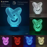 An LED 3D optical illusion knot lamp shown in multiple colour modes on a dark background. The main panel shows the lamp glowing cyan in solid state mode, with smaller panels demonstrating other available colours: White, Green, Purple, Red, Blue, and Yellow.