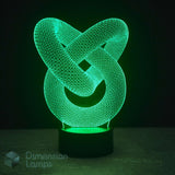 A 3D optical illusion LED lamp featuring an interlocking knot design that glows with a vibrant green light, set on a black cylindrical base against a dark background.