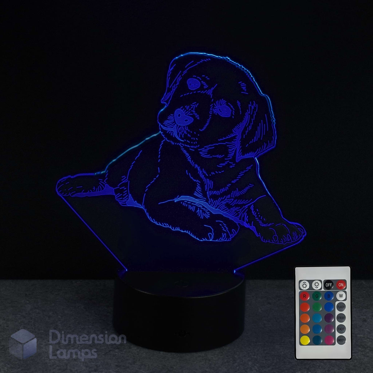 A 3D optical illusion night light shaped like a puppy, glowing with blue light on a black base, shown alongside a 16 colour remote control and a 'Dimension Lamps' logo watermark.