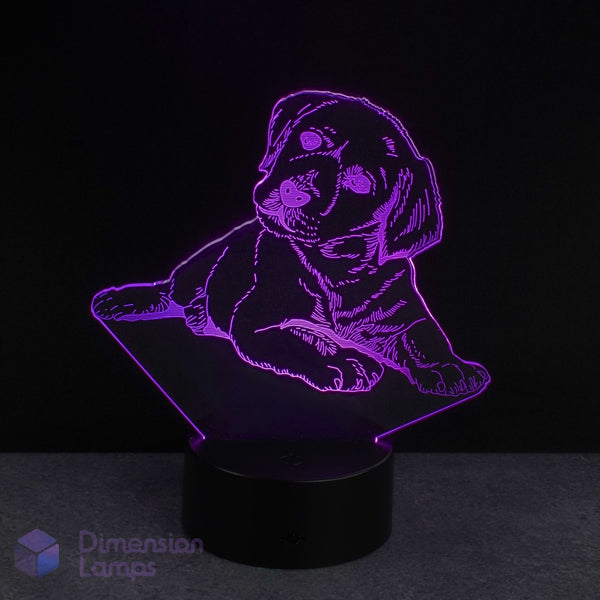 A 3D optical illusion LED night light shaped like a puppy, glowing with a purple light on a black base against a dark background. A 'Dimension Lamps' watermark is visible in the bottom-left corner.