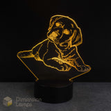 A 3D optical illusion night light shaped like a puppy lying down, glowing with a warm golden-yellow light from a black base. The brand name 'Dimension Lamps' is visible as a watermark in the bottom-left corner.