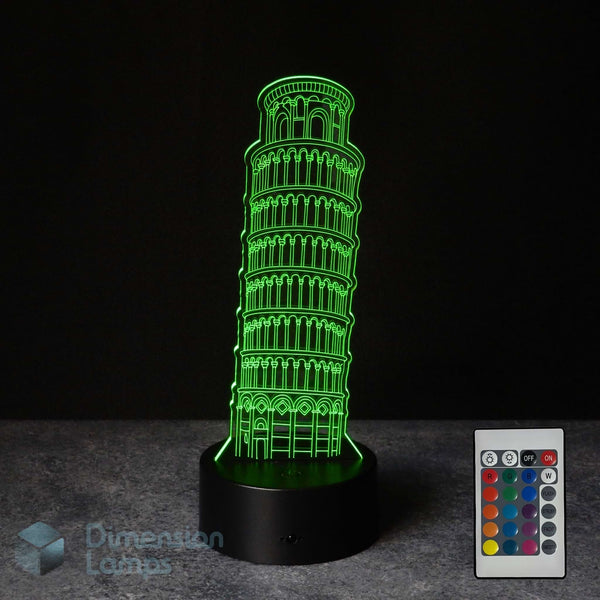 A 3D LED illusion lamp depicting the Leaning Tower of Pisa, glowing bright green on a black base, shown with a 16 colour remote control on a dark background.