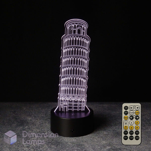 An LED 3D optical illusion night light shaped like the Leaning Tower of Pisa, glowing with a purple light on a black base, shown with the 7 colour remote control against a dark background.