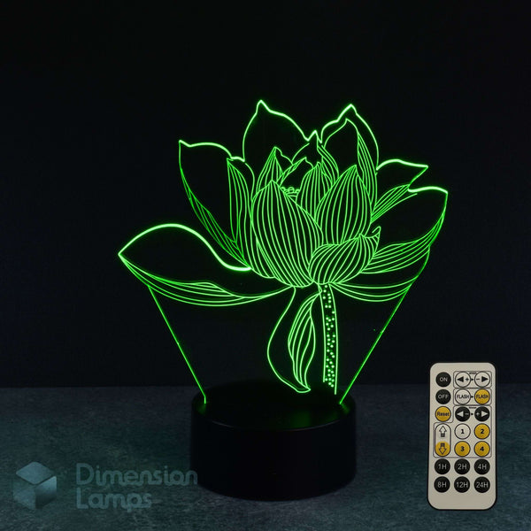 Viewed against a dark background, a 3D illusion lamp forms the shape of a green lotus flower, rising from a circular black base. Featuring a 7 colour remote control with sleep timer function.
