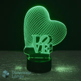 A 3D optical illusion LED night light shaped like a heart with the word 'LOVE' cut through it, glowing green on a black base against a dark background. A 'Dimension Lamps' watermark is visible in the lower-left corner.