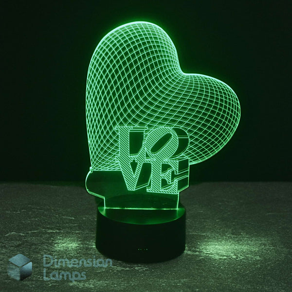A 3D optical illusion LED night light shaped like a heart with the word 'LOVE' cut through it, glowing green on a black base against a dark background. A 'Dimension Lamps' watermark is visible in the lower-left corner.
