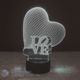 A 3D optical illusion LED night light shaped like a glowing heart with the word 'LOVE' integrated into the design, resting on a black cylindrical base against a dark background, making this an ideal girls gift idea. 