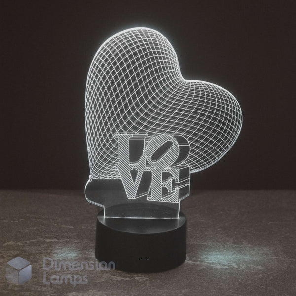 A 3D optical illusion LED night light shaped like a glowing heart with the word 'LOVE' integrated into the design, resting on a black cylindrical base against a dark background, making this an ideal girls gift idea. 