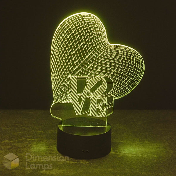 A 3D optical illusion LED lamp shaped like a heart with the word 'LOVE' cut through it, glowing green on a black base against a dark background.