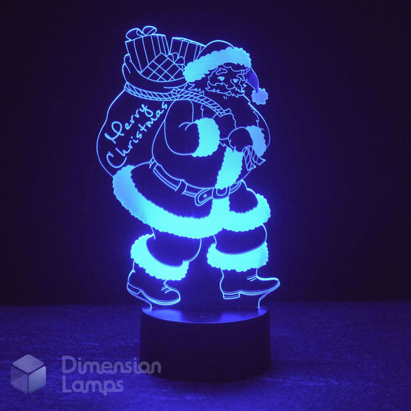 A 3D LED Santa Claus night light carrying a gift sack, glowing bright blue light on a dark base. The brand Dimension Lamps in the bottom-left corner.