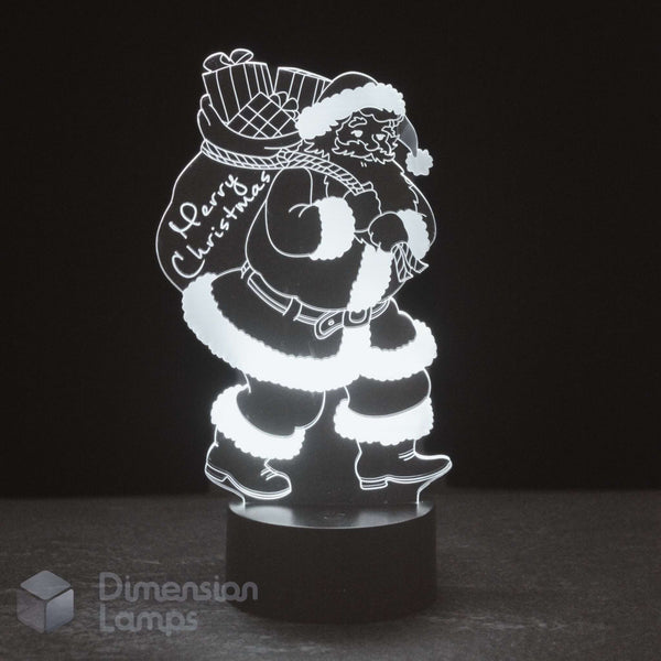 A glowing white LED night light of Santa Claus carrying a Christmas sack, on a black base against a dark background. And the words 'Merry Christmas'.