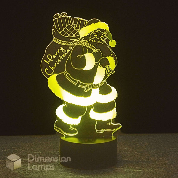 An LED 3D optical illusion night light of Santa Claus carrying a sack, glowing with a warm yellow light against a dark background. Christmas lighting.