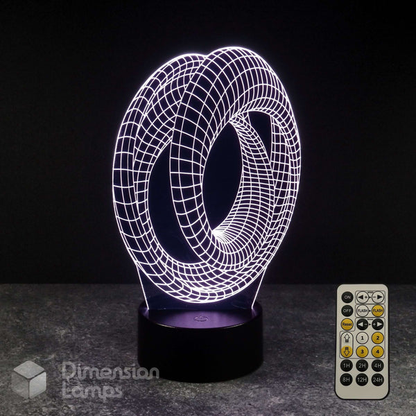 A 3D optical illusion LED night light with a glowing white wireframe mobius strip design on a black base, shown with its remote control on a dark grey surface against a black background. Sci-fi fan gift idea.