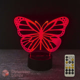 A red illuminated monarch butterfly-shaped LED night light on a black base, shown with a 7 colour remote control with sleep timer function against a dark background. Girls gift idea. 