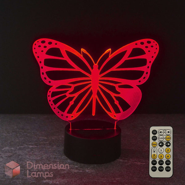 A red illuminated monarch butterfly-shaped LED night light on a black base, shown with a 7 colour remote control with sleep timer function against a dark background. Girls gift idea. 